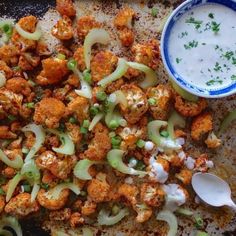 a plate filled with cauliflower and sauce next to a bowl of ranch dressing