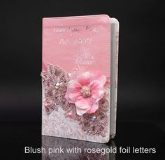 a pink and white wedding guest book with flowers on the front, sitting on a black surface