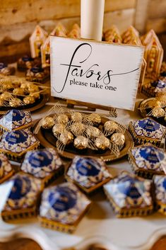 a table topped with blue and gold plates covered in cookies next to a sign that says fauss please take one