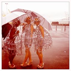 three women standing under an umbrella in front of the ocean with sparkling clothes on them