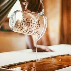 a person pouring water into a glass cup on top of a wooden table next to a window