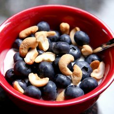 a red bowl filled with blueberries and cashews on top of a counter