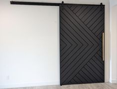 an empty room with a black door and wood flooring on the wall, next to a white wall