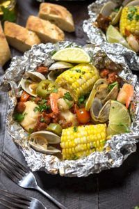 two tin foil bowls filled with seafood and corn on the cob next to bread