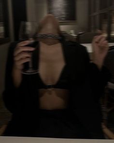 a woman sitting in a chair holding a wine glass up to her face with both hands