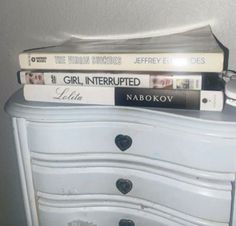 three books stacked on top of each other on a small white dresser in a bedroom