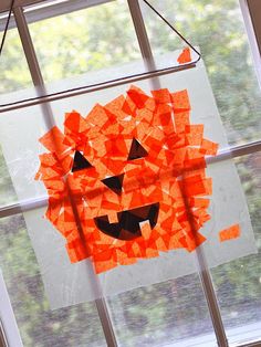 an orange pumpkin made out of pieces of construction paper hanging from a window sill