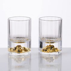 two glasses filled with gold nuggets on top of a white table next to each other