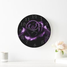 a black and purple rose clock sitting on top of a white table next to a vase with flowers