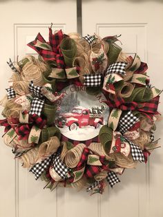 a christmas wreath with a red truck and plaid ribbon hanging on the front door,