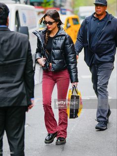 a woman in black jacket and red pants walking down the street with a man behind her