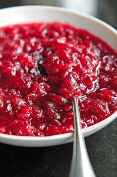 a white bowl filled with cranberry sauce on top of a black table next to a spoon