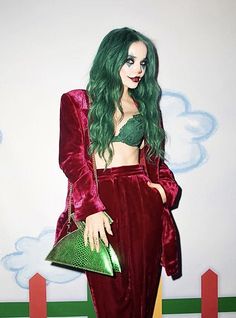 a woman with green hair wearing a red outfit and holding a green purse in front of a white wall