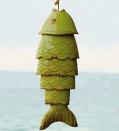 a green bird feeder hanging from the side of a body of water