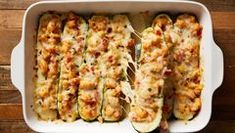 zucchini stuffed with meat and cheese in a white casserole dish on a wooden table