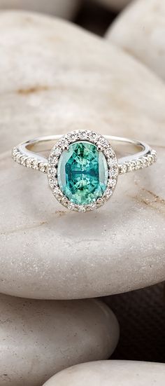 a ring with an oval cut blue topazte surrounded by small white diamonds sits on some rocks