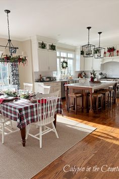 Kitchen table with plaid tablecloth in white kitchen with stained wood island all decorated with Christmas wreaths and bows.