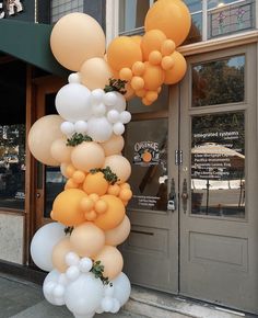 a bunch of white and orange balloons hanging from the side of a store front door