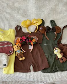 baby clothes and accessories laid out on a bed with a teddy bear in the middle