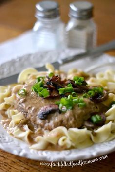 a white plate topped with pasta and meat covered in mushroom sauce on top of a wooden table