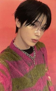 a woman with short black hair wearing a pink and green striped sweater is looking at the camera