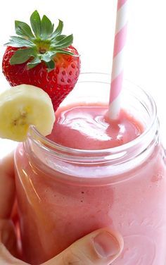 a hand holding a strawberry and banana smoothie in a mason jar with a straw