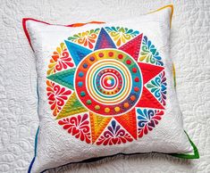 a colorful decorative pillow on a white quilt