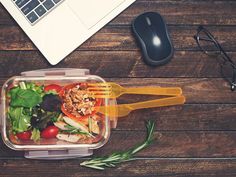 a plastic container filled with salad next to a computer mouse and eyeglasses on top of a wooden table