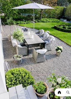 an outdoor dining table and chairs with umbrella in the middle of a graveled area