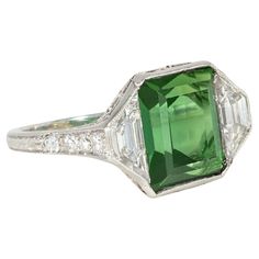 An Art Deco tourmaline, diamond, and platinum ring featuring an emerald-cut green tourmaline center flanked by trapezoid diamonds, with diamond-set shoulders and open scrolled foliate work in the gallery, in platinum. Marcus & Co. Atw tourmaline 4.61 cts., atw diamonds 1.75 cts. * Includes letter of authenticity for insurance purposes * Free shipping * Please do not hesitate to request additional photos of specific details or of this gorgeous period ring on a live model. Green Tourmaline Ring, Vintage Inspired Rings, Art Deco Diamond Rings, Platinum Diamond Rings, Jewels Rings, Three Stone Diamond, Fine Art Jewelry, Art Deco Engagement, Art Nouveau Jewelry