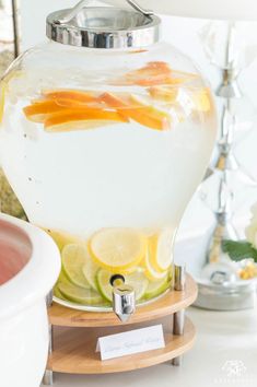 a fish bowl filled with lemons and water next to a white vase on a wooden stand