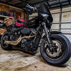 a black motorcycle parked in a garage next to a red and yellow helmet on it's back end