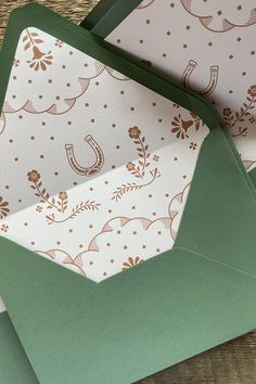 two green envelopes with gold foil designs on them, one opened and the other closed