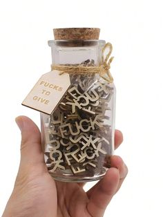 a hand holding a glass jar with letters in it and a tag on the top