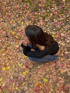 a woman sitting on the ground covered in leaves