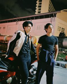 two young men standing next to each other near a parked motorbike in front of a building