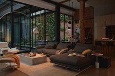 a living room filled with furniture next to a tall glass wall covered in greenery