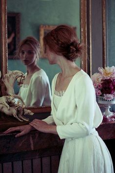 a woman standing in front of a mirror next to a vase with flowers on it