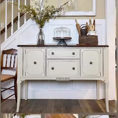 there is a white dresser with flowers on it in front of the stairs and table