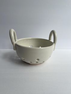 a white bowl with an animal shaped handle on the side and holes in the bottom