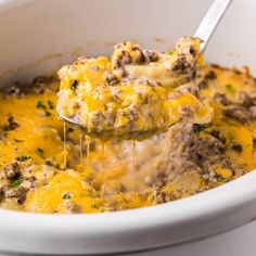 a spoon full of cheesy ground beef casserole being lifted from a white bowl