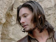 a man with long hair wearing a brown leather jacket and looking off to the side