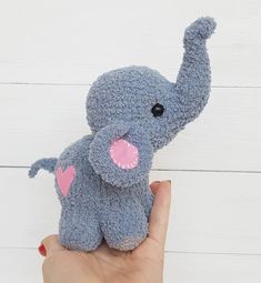 a hand holding a small stuffed elephant with pink heart on it's chest and tail