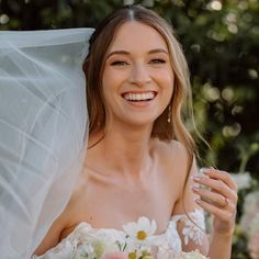 a woman in a wedding dress holding a bouquet of flowers and smiling at the camera