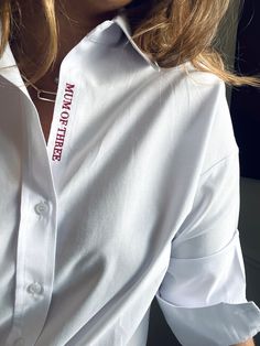 a woman wearing a white shirt with red lettering on the chest and collar is looking off to the side