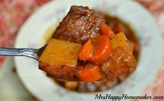 a spoon full of stew with carrots and potatoes on it in a white bowl