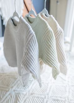 two knit sweaters hanging from hooks on a white bedspread in a bedroom