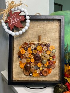 a wooden frame with buttons on it next to a wreath and fall leaves in the background