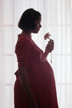 a pregnant woman in a red dress holding a flower