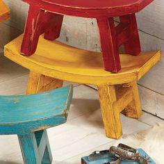 three colorful wooden stools sitting next to each other on top of a white floor